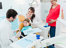 Dentiste en consultation avec une jeune patiente accompagnée de sa mère enceinte - MACSF