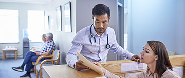 Un médecin discute d'un dossier avec sa secrétaire à l'accueil - MACSF