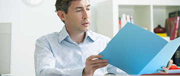 Un médecin, assis à son bureau, consulte un dossier médical - MACSF