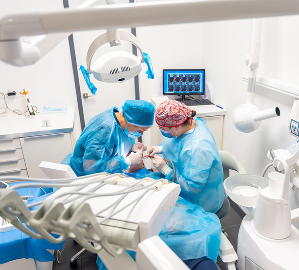 Deux chirurgiens-dentistes en tenue chirurgicale réalisent un acte d'implantologie - MACSF