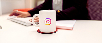 Gros plan sur un mug décoré sur logo instagram et en arrière plan le buste d'une femme qui a les mains posées sur son clavier - MACSF