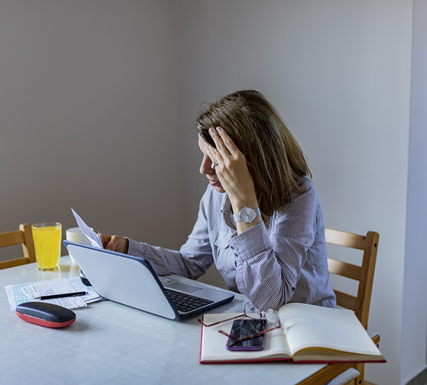 Femme inquiète consultant des papiers devant son ordinateur portable - MACSF
