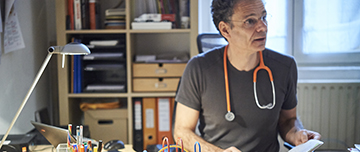 Un pédiatre assis à son bureau consulte le carnet de santé - MACSF