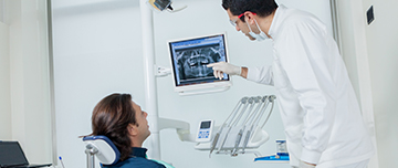 Le dentiste pointe une radio dentaire en expliquant les soins au patient - MACSF
