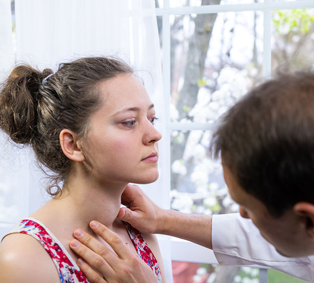 Une médecin examine le cou d’une femme en palpant sa gorge dans un cabinet médical - MACSF