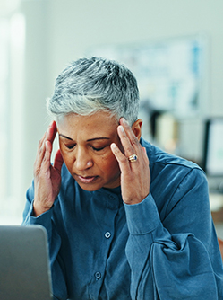 Une femme d'une cinquantaine d'années se tient les tempes devant sont pc portable - MACSF