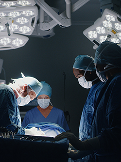 Equipe médicale exécutant une chirurgie, éclairée par les projecteurs d'une salle d'opération sombre - MACSF