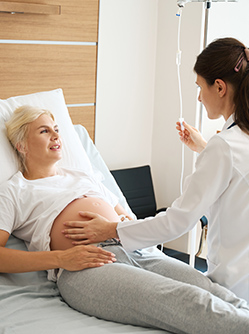 Une sage-femme examine une patiente enceinte allongée dans un lit d’hôpital  - MACSF