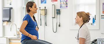 Une femme enceinte assise sur la table d'examen face à la sage-femme - MACSF