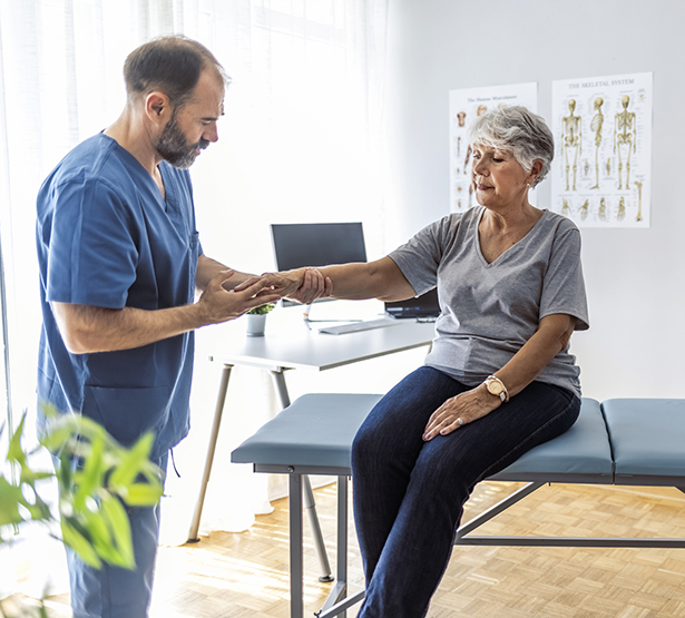 Le médecin examine le poignet d'une patiente âgée assise sur la table d'examen - MACSF