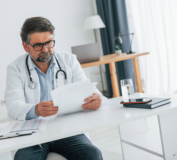 Un médecin installé à son bureau lit des documents - MACSF