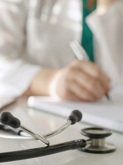 Un stéthoscope posé sur un bureau avec une professionnelle de santé qui prend des notes en arrière-plan - MACSF