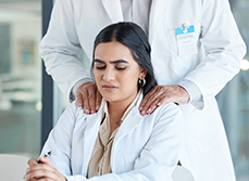 Soignante à son bureau, mal à l’aise, tandis qu’un collègue lui pose les mains sur les épaules - MACSF