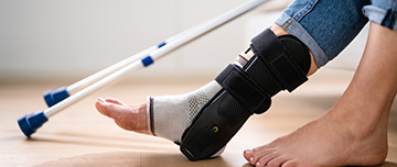 Une personne porte une attelle de cheville, avec des béquilles visibles en arrière-plan - MACSF