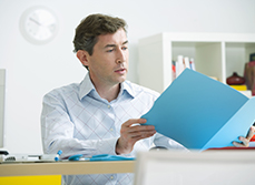 Un médecin, assis à son bureau, consulte un dossier médical - MACSF