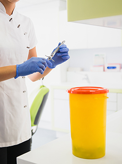 Une technicienne de cabinet dentaire s'apprête à mettre une seringue dans un bac à déchets médicaux - MACSF