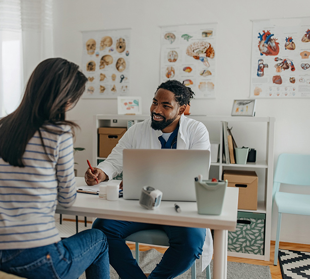 Un médecin souriant assis face à sa patiente prend des notes - MACSF