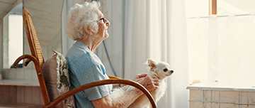 Une femme âgée regarde par la fenêtre avec son chien sur les genoux - MACSF