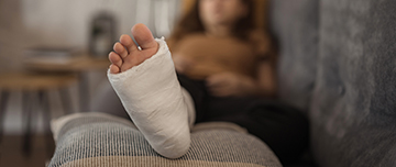 Gros plan sur le pied d'une femme en arrière plan à la jambe plâtrée allongée dans son canapé - MACSF
