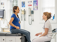 Une femme enceinte assise sur la table d'examen face à la sage-femme - MACSF