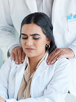 Soignante à son bureau, mal à l’aise, tandis qu’un collègue lui pose les mains sur les épaules - MACSF