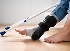 Une personne porte une attelle de cheville, avec des béquilles visibles en arrière-plan - MACSF