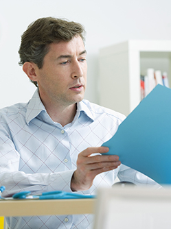 Un médecin, assis à son bureau, consulte un dossier médical - MACSF