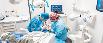 Deux chirurgiens-dentistes en tenue chirurgicale réalisent un acte d'implantologie - MACSF