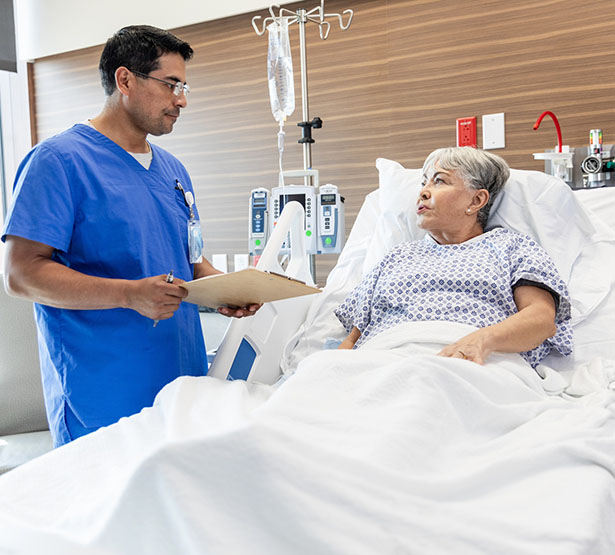 Une patiente dans son lit d'hopital discute avec un soignant tenant un dossier médical - MACSF