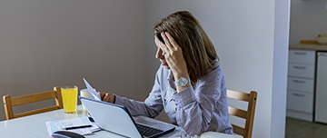 Femme inquiète consultant des papiers devant son ordinateur portable - MACSF