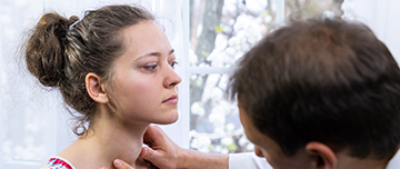Une médecin examine le cou d’une femme en palpant sa gorge dans un cabinet médical - MACSF