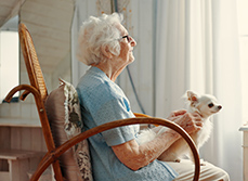 Une femme âgée regarde par la fenêtre avec son chien sur les genoux - MACSF