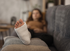 Gros plan sur le pied d'une femme en arrière plan à la jambe plâtrée allongée dans son canapé - MACSF