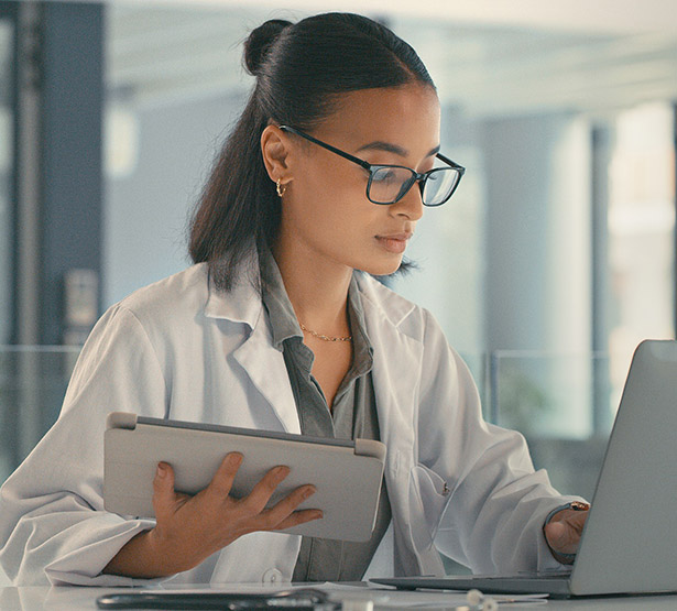 Une femme médecin face à son ordinateur tenant à la main une tablette - MACSF