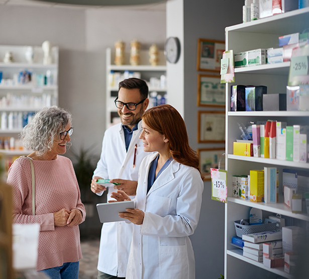 Deux pharmaciens souriants conseillent une cliente âgée - MACSF