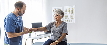 Le médecin examine le poignet d'une patiente âgée assise sur la table d'examen - MACSF