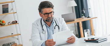Un médecin installé à son bureau lit des documents - MACSF
