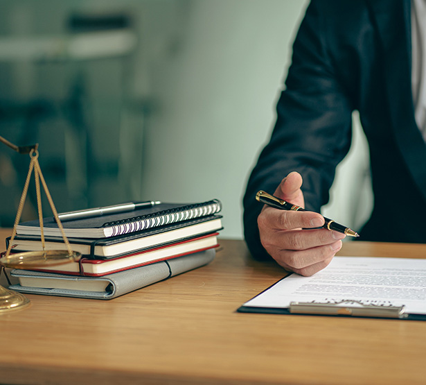 Gros plan sur une main d'homme s'apprêtant à écrire, avec à droite une pile de carnets et une balance de la justice - MACSF