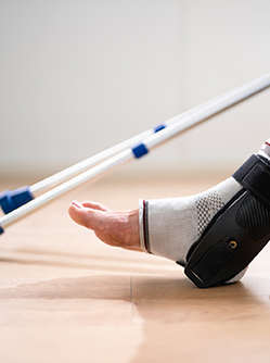 Une personne porte une attelle de cheville, avec des béquilles visibles en arrière-plan - MACSF