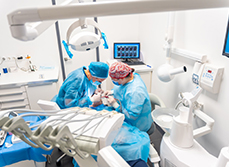 Deux chirurgiens-dentistes en tenue chirurgicale réalisent un acte d'implantologie - MACSF