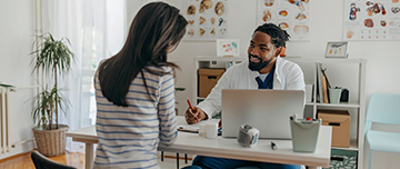 Un médecin souriant assis face à sa patiente prend des notes - MACSF