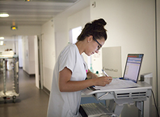 Un infirmière remplissant un dossier posé sur le chariot dans le couloir de l'hôpital - MACSF