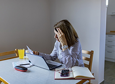 Femme inquiète consultant des papiers devant son ordinateur portable - MACSF