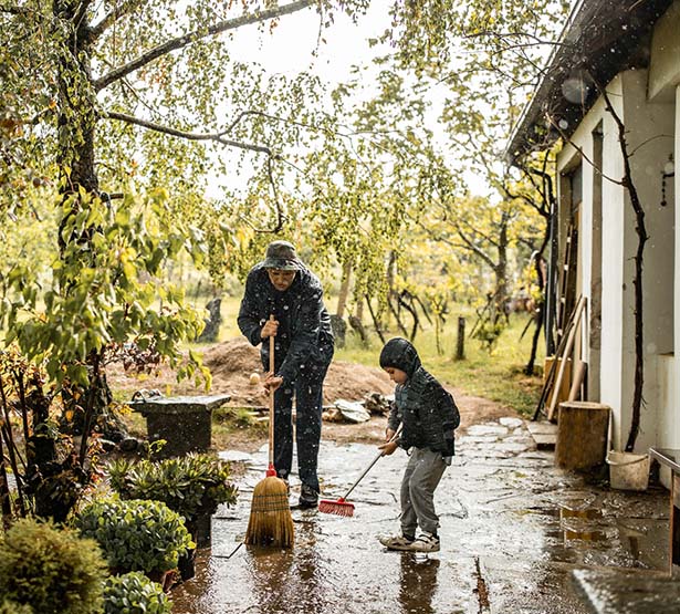 Un père et son enfant balayent une terrasse après une grosse pluie - MACSF