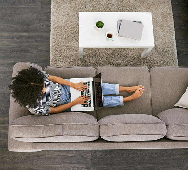 Une femme installée sur son canapé consulte son PC - MACSF