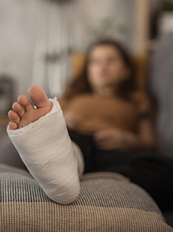 Gros plan sur le pied d'une femme en arrière plan à la jambe plâtrée allongée dans son canapé - MACSF
