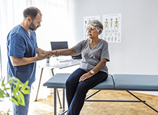 Le médecin examine le poignet d'une patiente âgée assise sur la table d'examen - MACSF