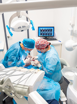 Deux chirurgiens-dentistes en tenue chirurgicale réalisent un acte d'implantologie - MACSF