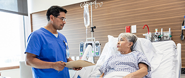 Une patiente dans son lit d'hopital discute avec un soignant tenant un dossier médical - MACSF