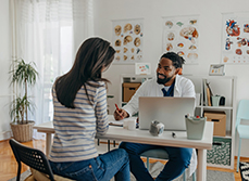 Un médecin souriant assis face à sa patiente prend des notes - MACSF
